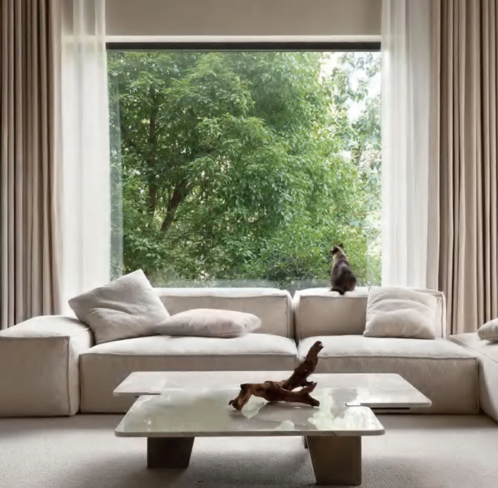 Bright living room with a cream coloured, sofa, table and curtains.