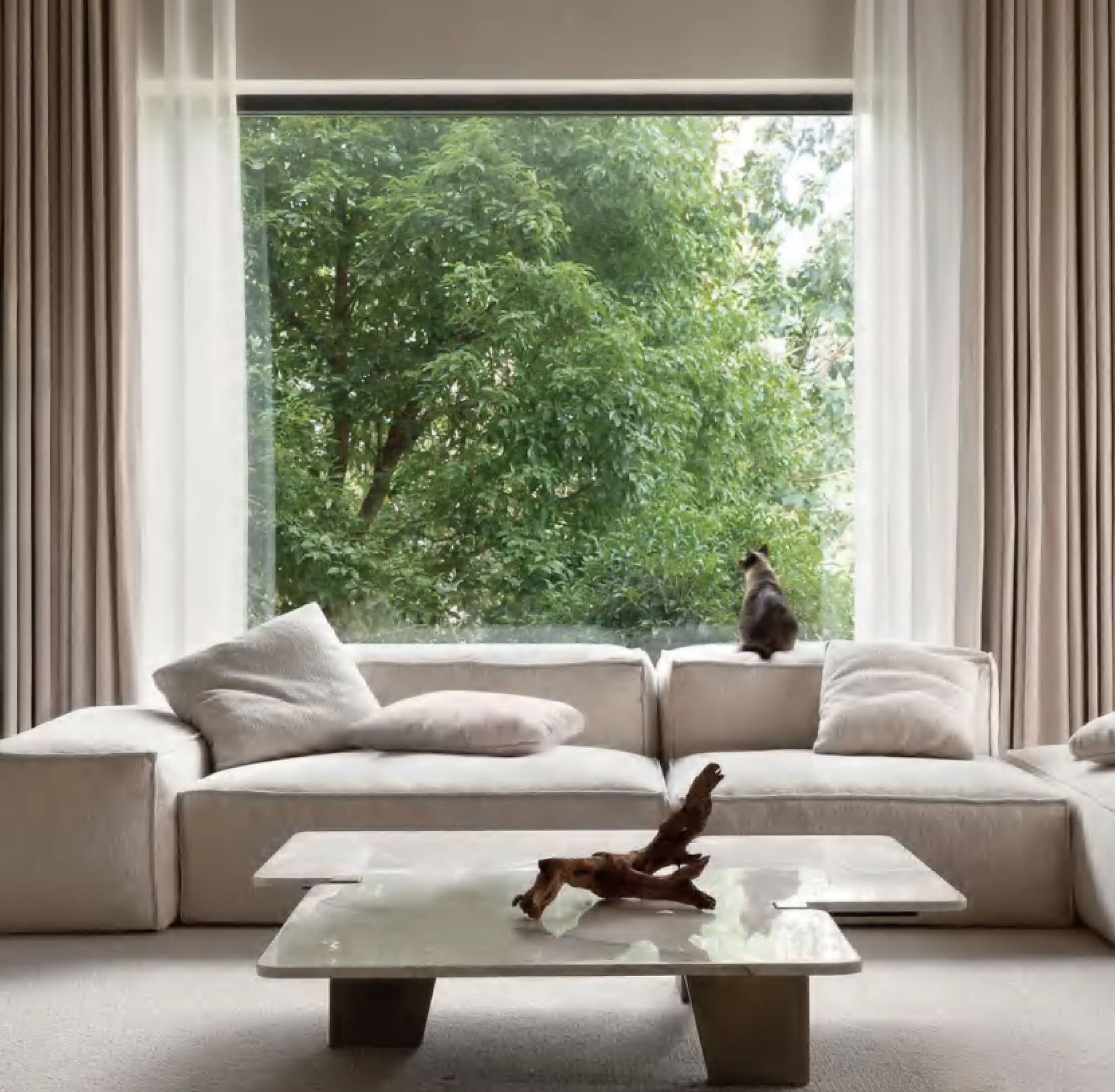 Bright living room with a cream coloured, sofa, table and curtains.